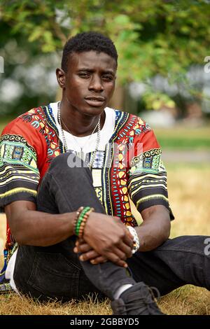 Un uomo africano in abiti nazionali sudafricani, un giovane nero che riposa in un parco in abiti nazionali Foto Stock