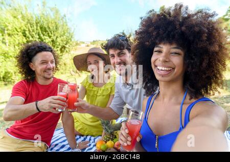 gruppo vario di persone che sedurono le vacanze estive in un picnic all'aperto facendo un ritratto selfie. amici multicultuali divertirsi bevendo e mangiando Foto Stock