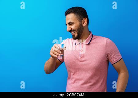 Bell'uomo ispanico che beve un bicchiere d'acqua fresca su sfondo blu Foto Stock