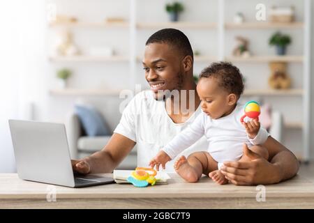 Congedo di paternità. Black Man che usa il computer portatile a casa e il bambino neonato Foto Stock