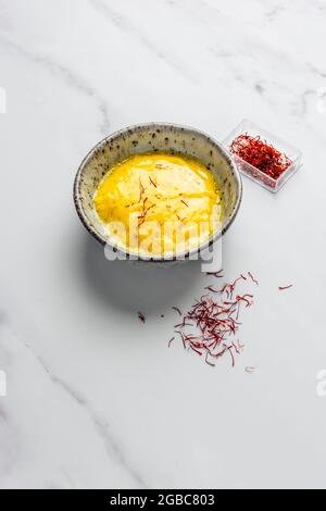 Rouille con fili di zafferano trefoli su marmo Bianco di fondo con confezione di zafferano sullo sfondo – FOODPIX BIANCO Foto Stock