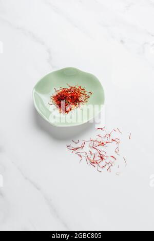 Fili di zafferano trefoli su sfondo bianco marmo con confezione di zafferano sullo sfondo – FOODPIX BIANCO Foto Stock