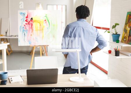 Pittore afroamericano maschile al lavoro guardando opere d'arte in studio d'arte Foto Stock