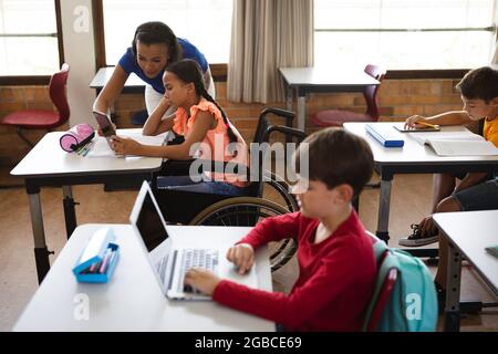 Insegnante femminile afroamericana che insegna alle ragazze disabili di usare il tablet digitale alla scuola elementare Foto Stock