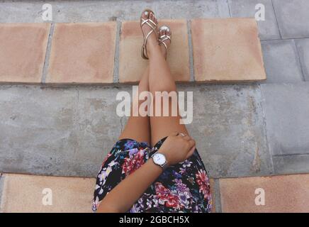 Donna con gonna floreale blu bianca e rossa con sandali in pelle marrone Foto Stock