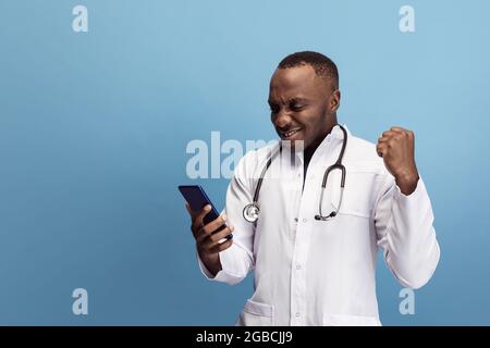 Giovane medico africano, consulente terapeutico o medico che posa isolato su sfondo blu studio. Divertenti emozioni meme. Concetto di assistenza sanitaria, assistenza Foto Stock