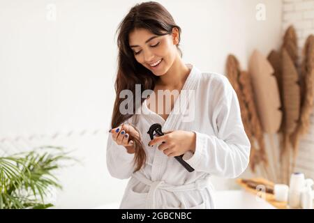 Brunette Lady spray Hairspray sulle estremità split in bagno moderno Foto Stock