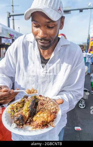 Miami Florida,Little Haiti,Caribbean Market Place Carnival Community Black man mangiare gustando piatto di cibo pollo alla griglia di manzo riso, Foto Stock