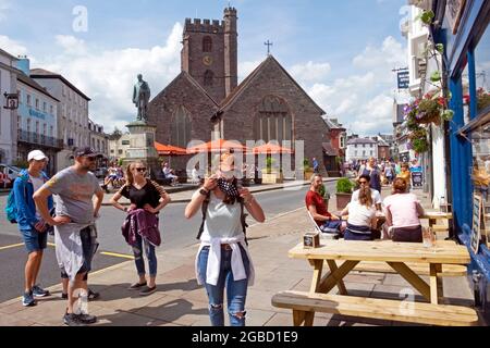 Donna mette sulla maschera covid al di fuori del ristorante staycation 2021 & famiglia in attesa di sedersi al tavolo da picnic nel centro di Brecon Galles UK KATHY DEWITT Foto Stock