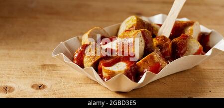 Delizioso piatto fast food di currywurst con ketchup e curry secco in ciotola per andare su sfondo marrone Foto Stock