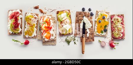 Dall'alto di vari gustosi toast croccanti con verdure e frutta messi in fila su sfondo bianco per uno spuntino sano Foto Stock