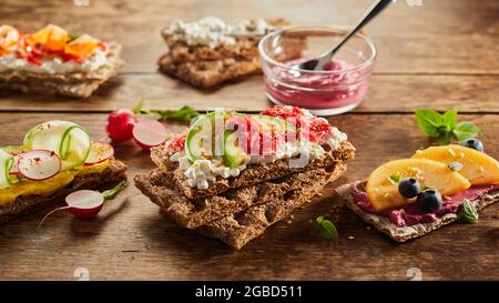 Ampia scelta di toast assortiti di croccanti con frutta e verdure gustose servite su un tavolo di legno per uno spuntino vegetariano Foto Stock