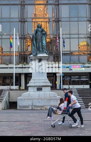 Inghilterra, Hampshire, Portsmouth, Guildhall Square, studenti universitari che spingono il supermercato Shopping Trolly di fronte alla statua della Regina Victoria Foto Stock