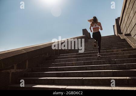 Signora sportiva in tuta corre su vecchi gradini di pietra sotto il cielo limpido Foto Stock