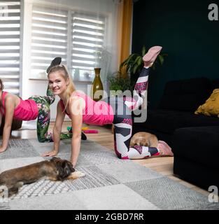 Due ragazze che si esercitano sollevano la gamba sinistra destra e le loro mani poggiano sul pavimento. Fitness in soggiorno. Foto Stock