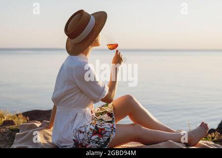 Bella signora in cappello di paglia con un bicchiere di vino sulla spiaggia. Foto Stock