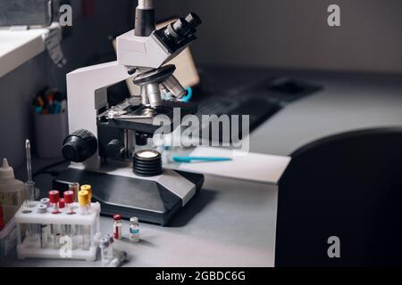 Microscopio, rack con provette e fiale su tavolo in laboratorio Foto Stock