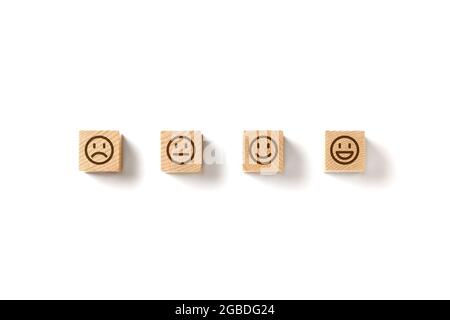 Emoticon facce in blocchi di legno su sfondo bianco. Valutazione del servizio e analisi della soddisfazione. Arrabbiato, neutro, buon umore e felice. Copia Foto Stock