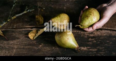 Alto angolo di raccolto maschio senza volto con fresche pere gustose posto su tavola di legno di shabby in cucina rustica Foto Stock