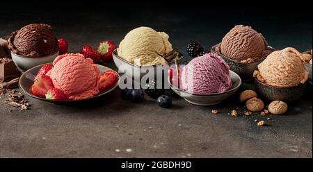 Set di appetitosi bicchierini di gelato di vari colori e favori con cioccolato e bacche in ciotole Foto Stock