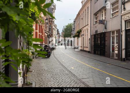 Breda, Paesi Bassi 28 giugno 2021. Strada nel centro della città con vecchi edifici storici, un marciapiede, negozi, case, un ciclista, biciclette parcheggiate Foto Stock