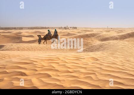 Vista dei turisti che cavalcano i cammelli nel deserto del Sahara durante i forti venti Foto Stock