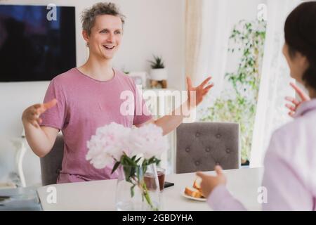 Giovane uomo e donna discutono emozionalmente qualcosa nella cucina domestica. Coppia con colazione e divertimento insieme. Tempo di famiglia. Foto Stock