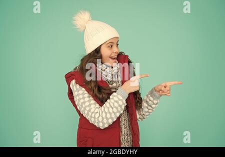 ragazza allegra in strati di vestiti che poiting dito. copia spazio. abiti caldi durante la stagione invernale. previsioni del tempo freddo. capretto shopping di moda. xmas Foto Stock