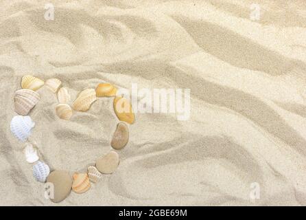 Heart on Sea Sand da ciottoli e conchiglie per lo sfondo Foto Stock