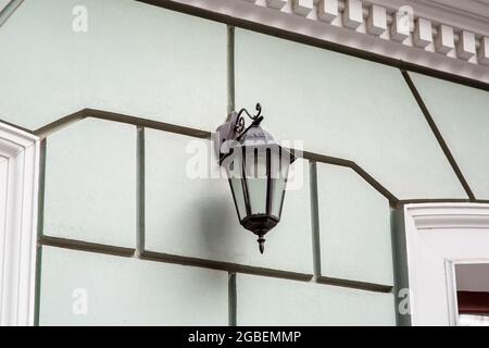 lanterna in ferro nero appesa per illuminazione stradale retrò con lampadina elettrica e paralume trasparente in vetro sulla facciata della parete dell'edificio con rustication pa Foto Stock