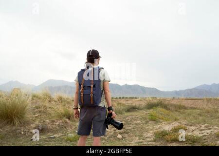 vista posteriore di un fotografo asiatico con zaino che guarda la vista con la fotocamera in mano Foto Stock