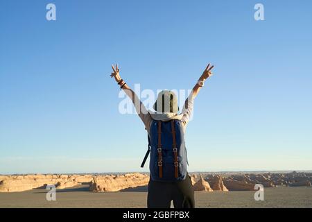 vista posteriore della donna asiatica zaino in spalla guardando la vista della terra yardang nel deserto di gobi, braccio esteso Foto Stock