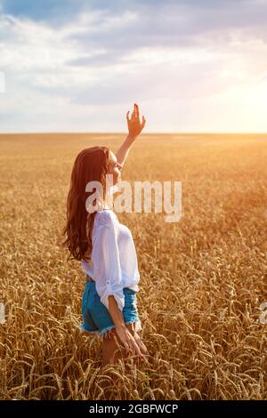 Le mani femminili si levano fuori dal campo di grano. Felice giovane donna è libera in un campo di grano dorato maturo. Passeggiate nella natura Foto Stock
