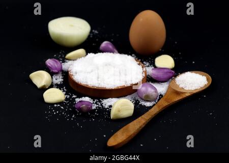Sale, cipolla, uovo e cucchiaio di legno su fondo nero Foto Stock
