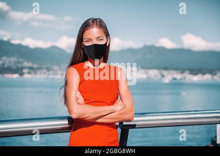Donna d'affari asiatica che indossa la maschera facciale come prevenzione del coronavirus. Fidata donna d'affari multirazziale fuori ritratto sorridente durante pandemia dentro Foto Stock