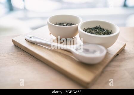 Selezione di tè verde di foglie cinesi sfuse secche dalla Cina per la degustazione a casa. Vassoio in legno con cucchiaio e tazze Foto Stock