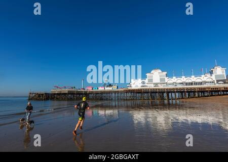 Inghilterra, Hampshire, Portsmouth, Southsea, Woman Walking Dogs e Jogger on Beach a Low Tide di fronte al molo di Southsea Foto Stock