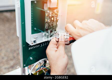 Regolazione dell'apparecchiatura di controllo e misurazione. Le mani di un elettricista o di un ingegnere con pinze al lavoro da vicino. L'appaltatore esegue i lavori nello stabilimento di produzione. Foto Stock