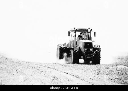 Grodno - Aprile 2021: Coltivazione di trattori agricoli in campo in nuvole di polvere immagine in bianco e nero ad alto contrasto. Fattoria di messa a fuoco selettiva Foto Stock