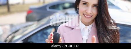 Giovane donna che tiene le chiavi dell'automobile e che mostra il pollice in su Foto Stock