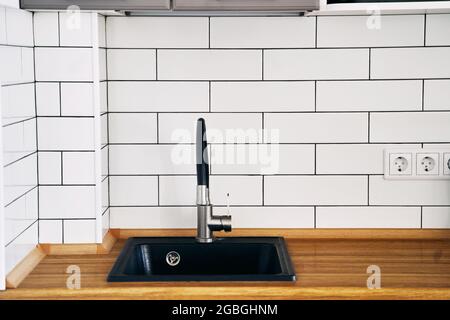 Elegante lavello nero e rubinetto su un piano di legno in una cucina da vicino Foto Stock