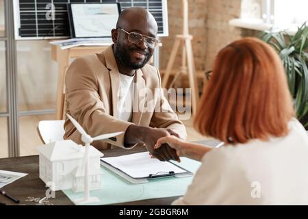 Uomo d'affari africano sorridendo e scuotendo la mano con il suo partner durante il loro incontro in ufficio Foto Stock
