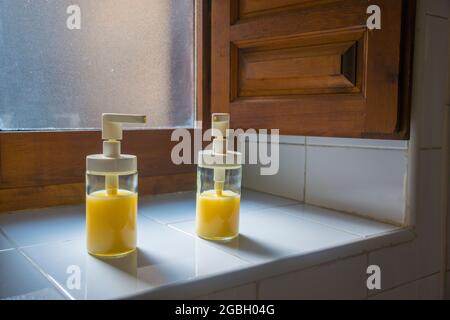 Due bottiglie di vetro con sapone liquido su una finestra. Foto Stock