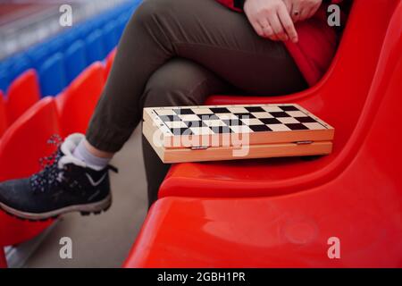 Primo piano di scacchi su stadio bleacher. Parte del corpo di una donna irriconoscibile che gioca nel gioco da tavolo a basse temperature. Foto Stock