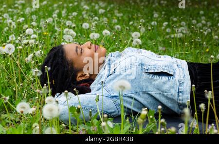 Ritratto di una giovane donna afro che giace nell'erba verde tra fiaccole e sorrisi. Vita felice. Foto Stock