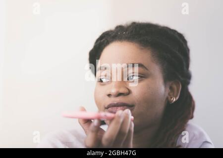 Triste donna di razza africana parla con smartphone mentre lo tiene davanti al viso. Colore classificato Foto Stock