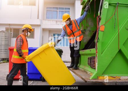 Due spolverini in piedi da un camion della spazzatura che svuota i bidoni della ruota, Thailandia Foto Stock