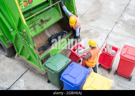 Due spolverini in piedi da un camion della spazzatura che svuota i bidoni della ruota, Thailandia Foto Stock