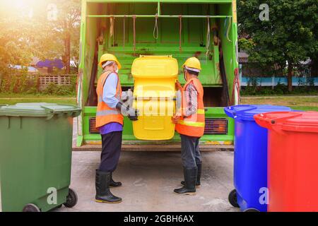 Due spolverini in piedi da un camion della spazzatura che svuota i bidoni della ruota, Thailandia Foto Stock