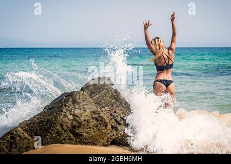 Vista posteriore di una donna in un bikini in piedi in mare surf con le mani in aria, spiaggia di Punta Paloma, Tarifa, Cadice, Andalusia, Spagna Foto Stock